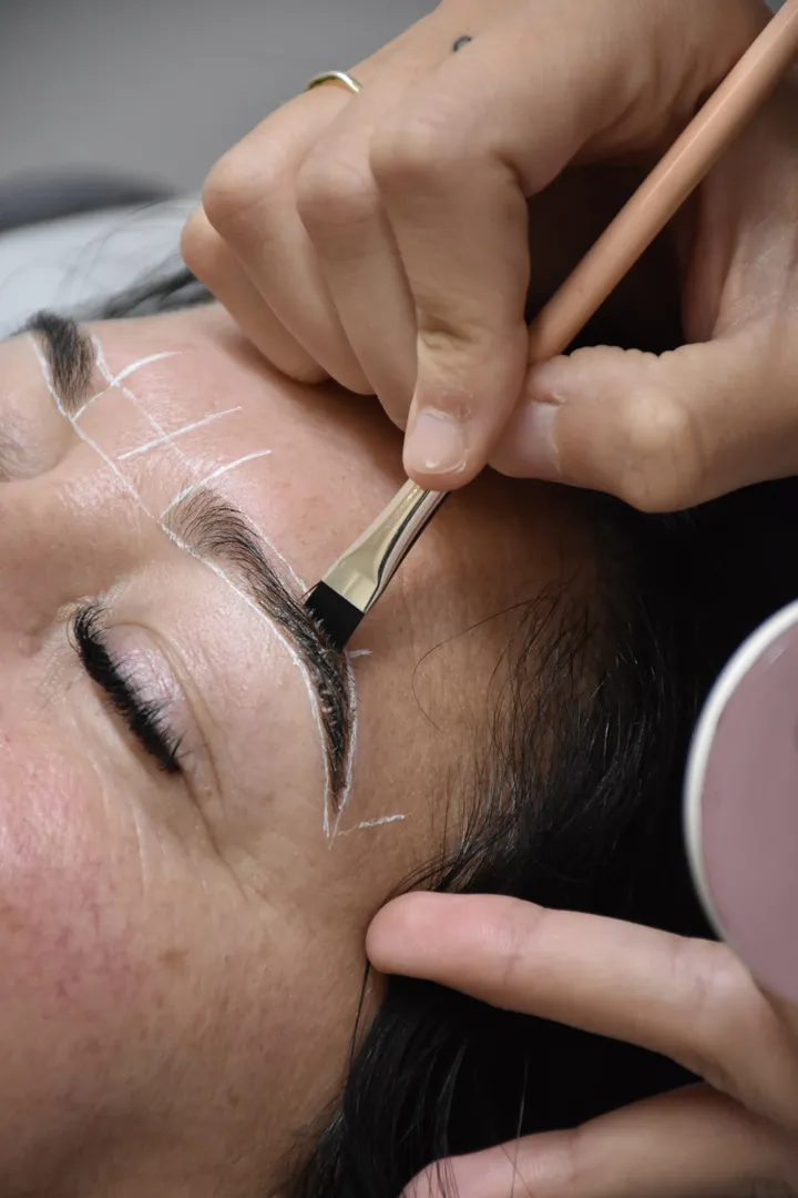 Microblading eyebrow preparation with brush and white markings.